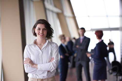 Smilling young business woman in front her team blured in background. Group of young business people. Modern bright startup office interior. Smilling young business woman in front her team blured in background. Group of young business people. Modern bright startup office interior.